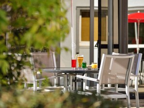 An outdoor seating area with a table and chairs, a drink menu, and a red umbrella in the background. - ibis Angouleme Nord (Champniers)