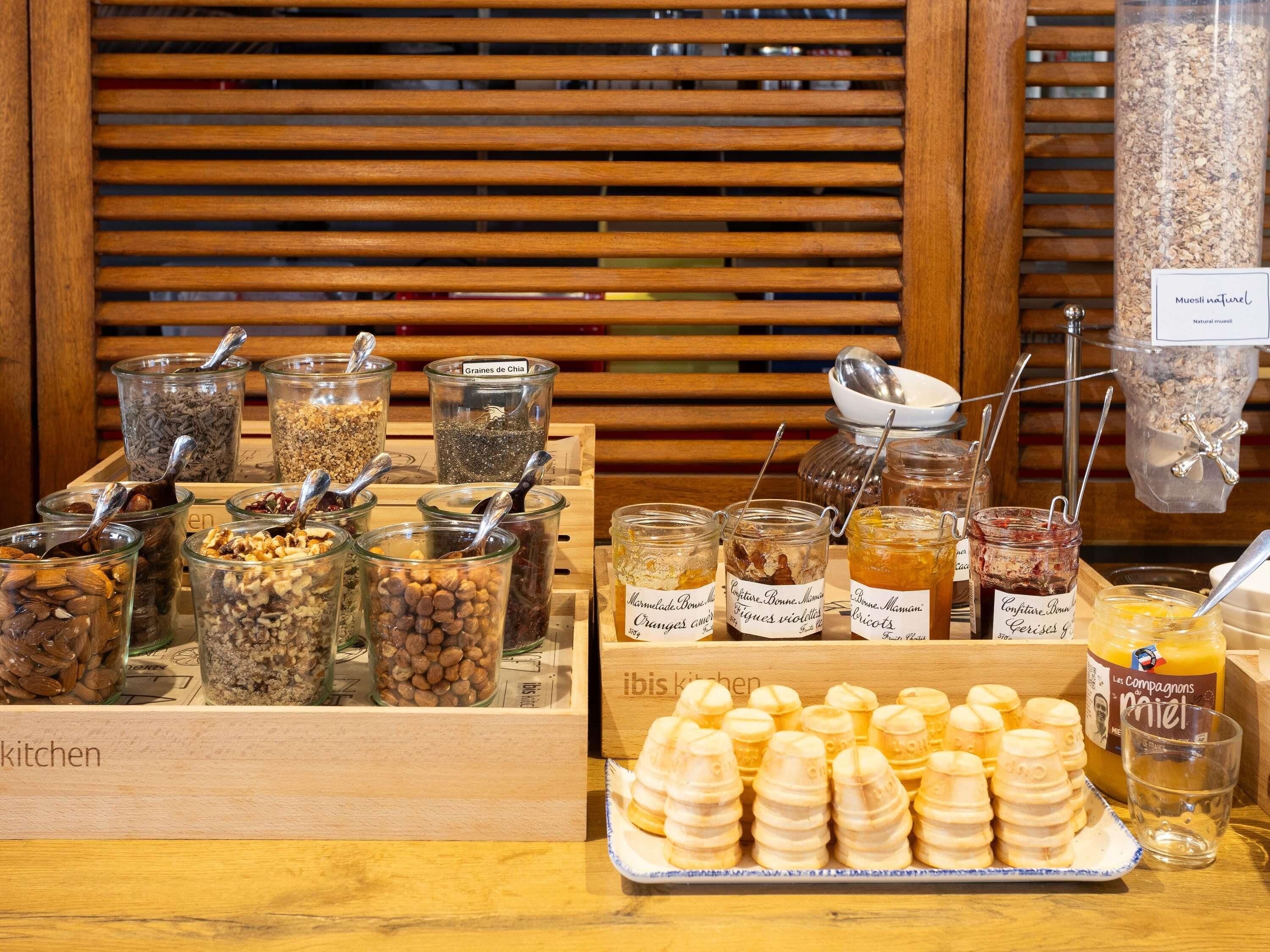 A variety of food items in glass jars with labels, a tray of cookies, and a glass of juice on a wooden table.