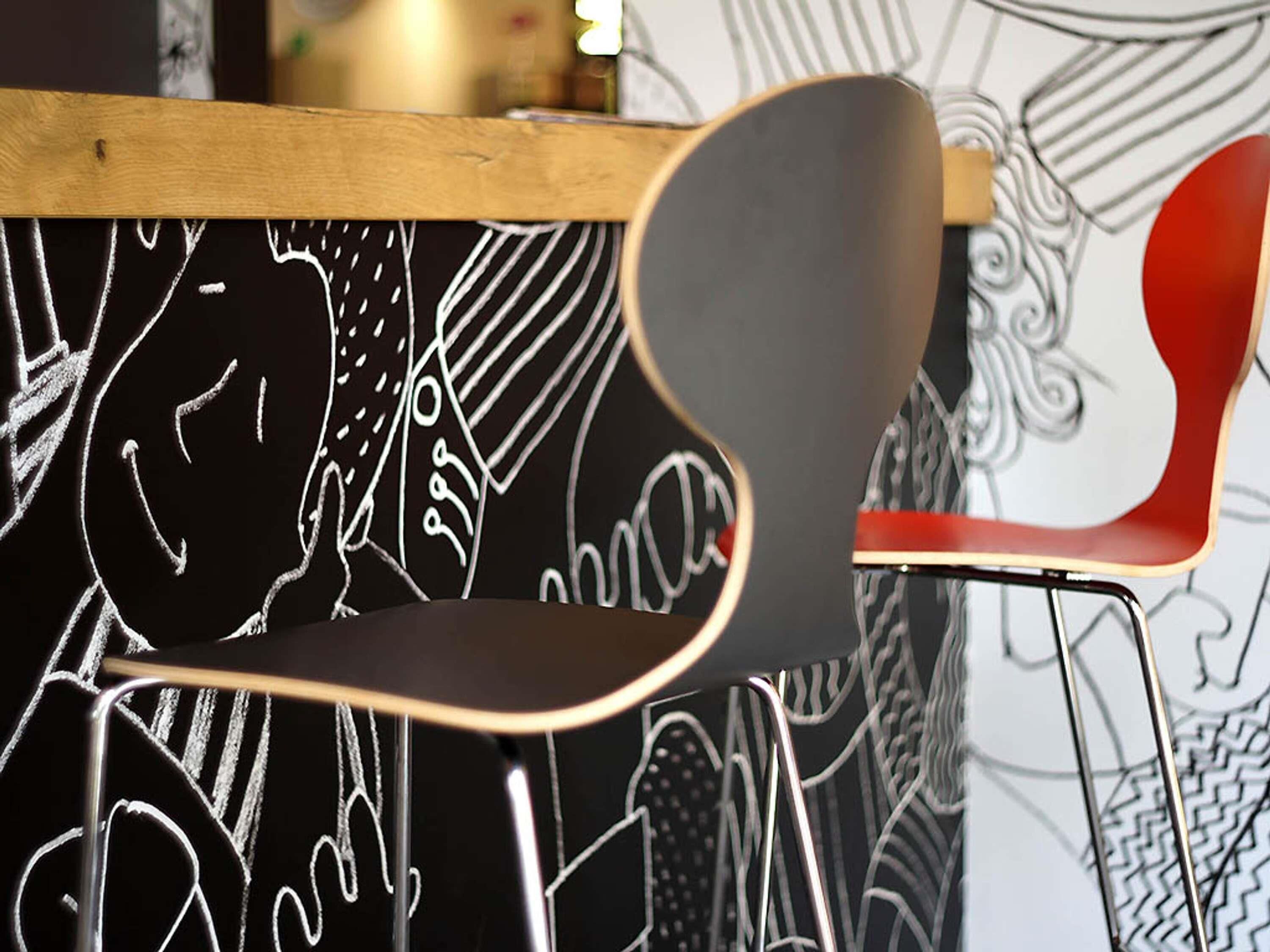 Une chaise dotée d’un dossier incurvé et de pieds en métal, placée devant un mur orné de dessins abstraits en noir et blanc.