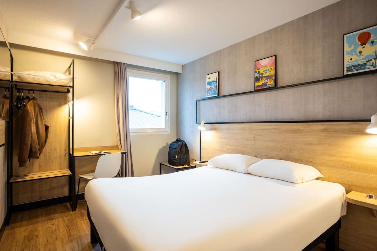 A hotel room with a large bed, a desk, a wardrobe, and a window with curtains.