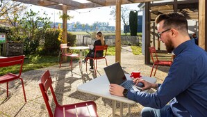 A covered outdoor seating area with wooden beams, red chairs, and a table with a laptop and a red cup. - ibis Angouleme Nord (Champniers)