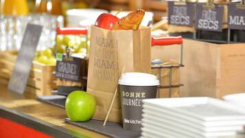 A food display with a paper bag, a croissant, an apple, and a coffee cup.