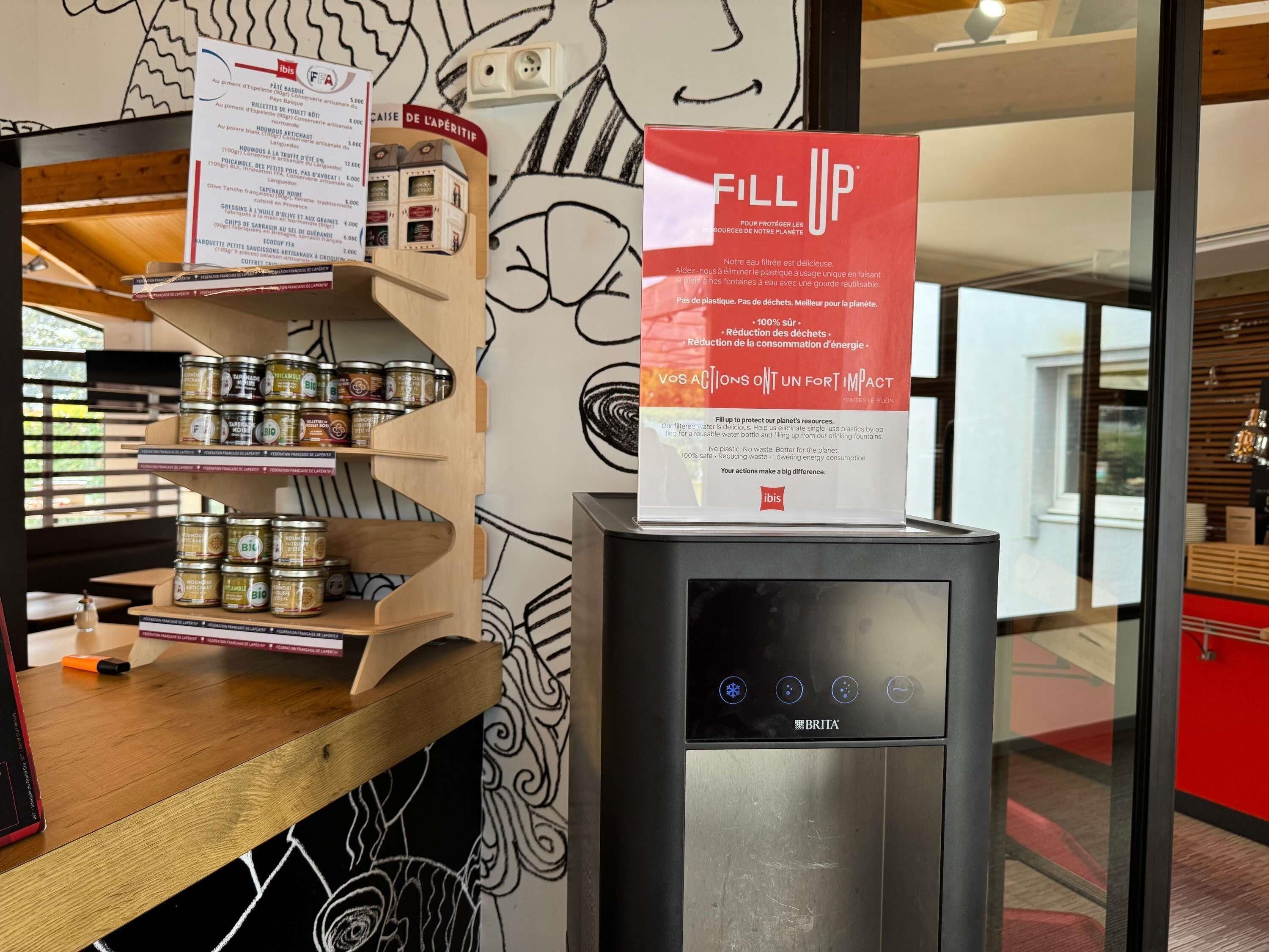 A kitchen area with a wooden shelf displaying canned goods, a water dispenser, and a menu board.
