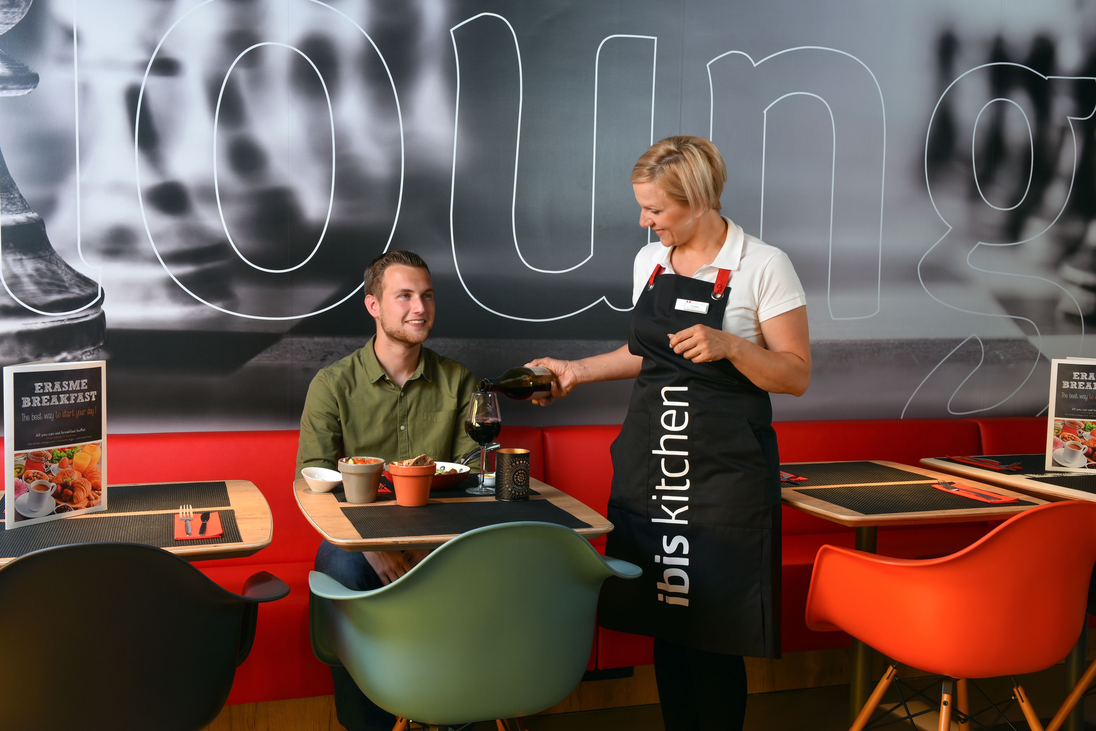 A restaurant interior with a red booth seating, a table with a menu, and a person pouring a drink.