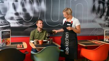 A restaurant interior with a red booth seating, a table with a menu, and a person pouring a drink.