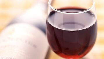A wine glass filled with red wine, placed next to a wine bottle.