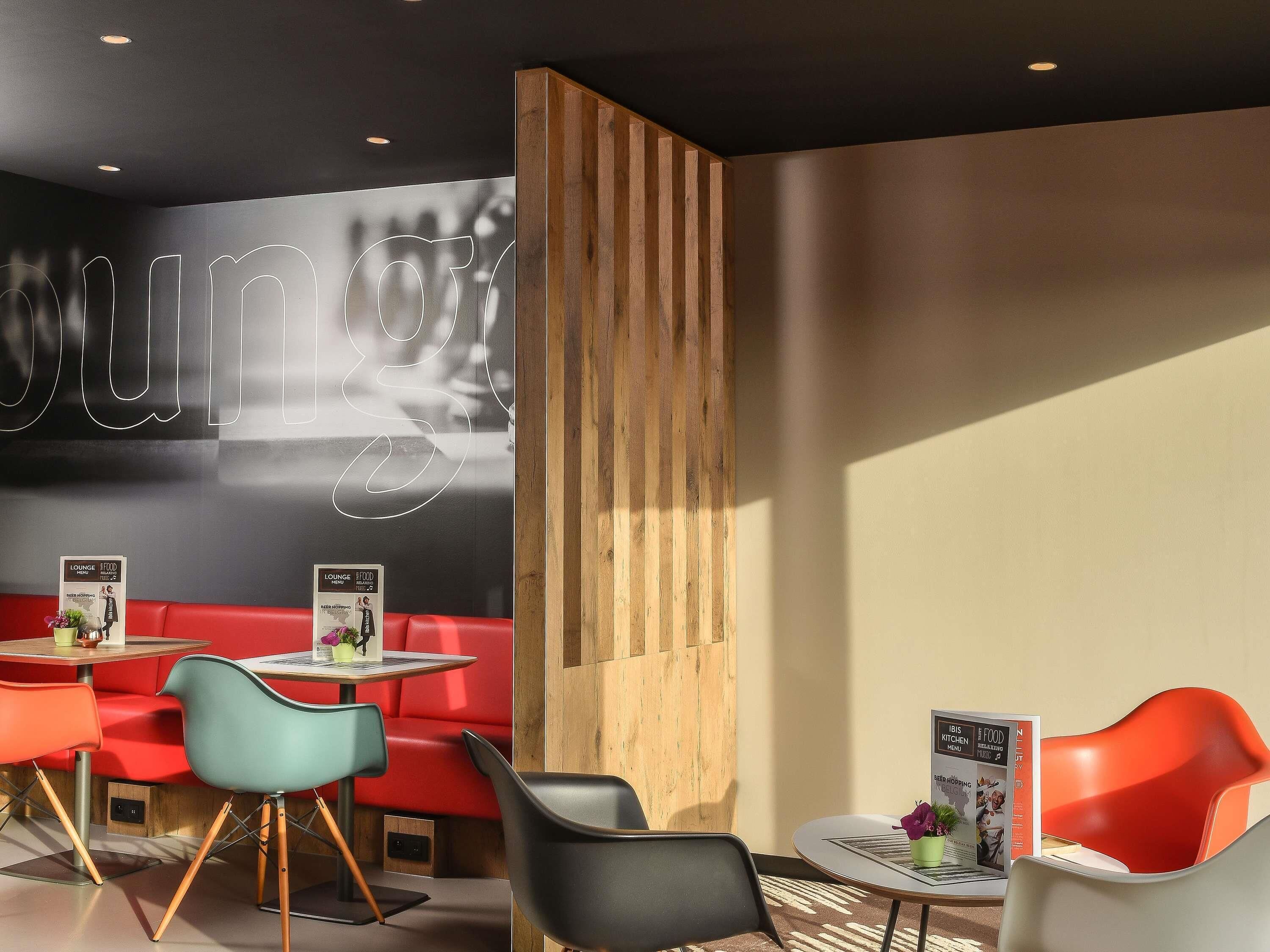Un espace lounge moderne avec des sièges rouges, un mur d’accent en bois et un panneau lumineux au néon.