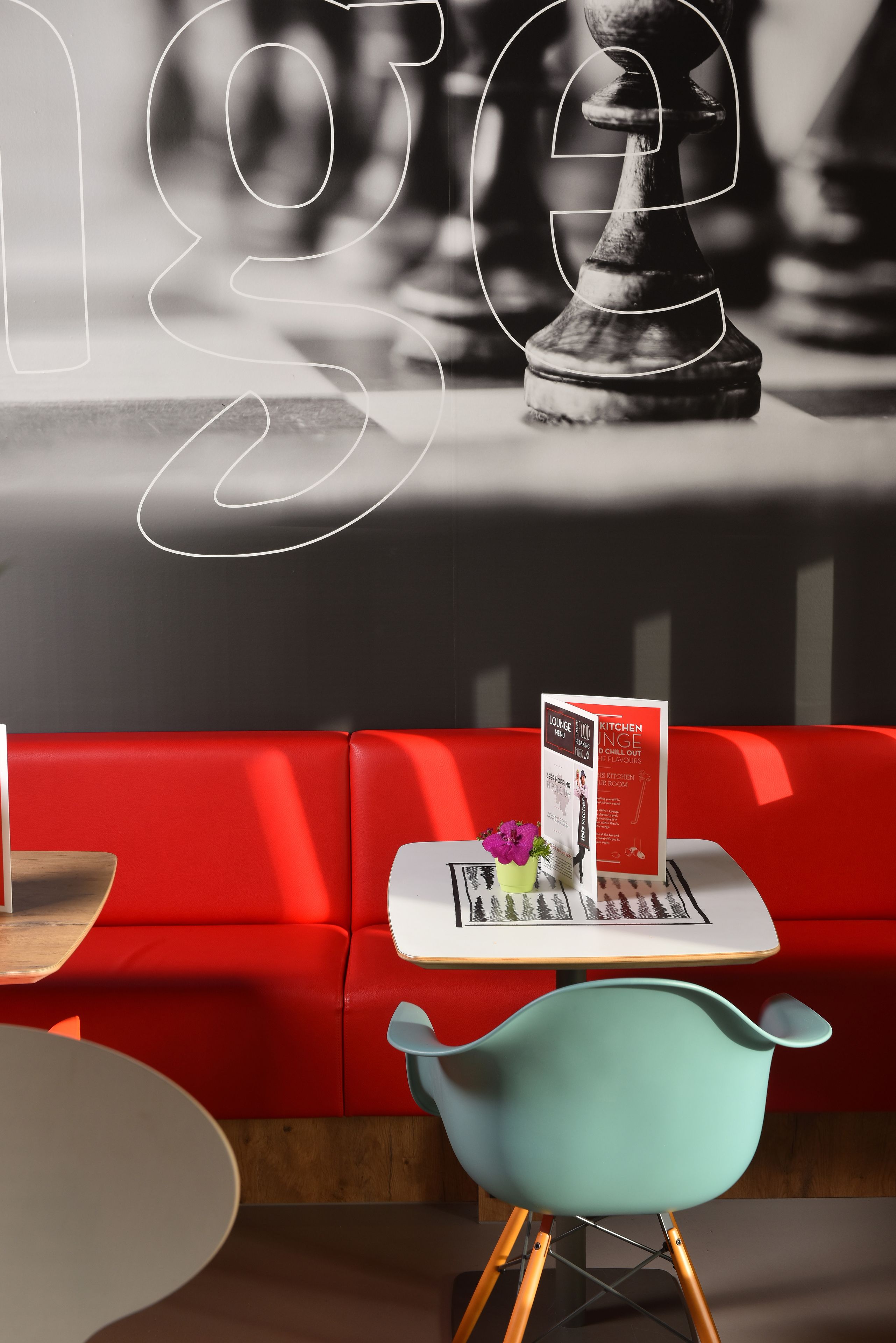 A modern interior with a red sofa, a teal chair, and a table with a menu.