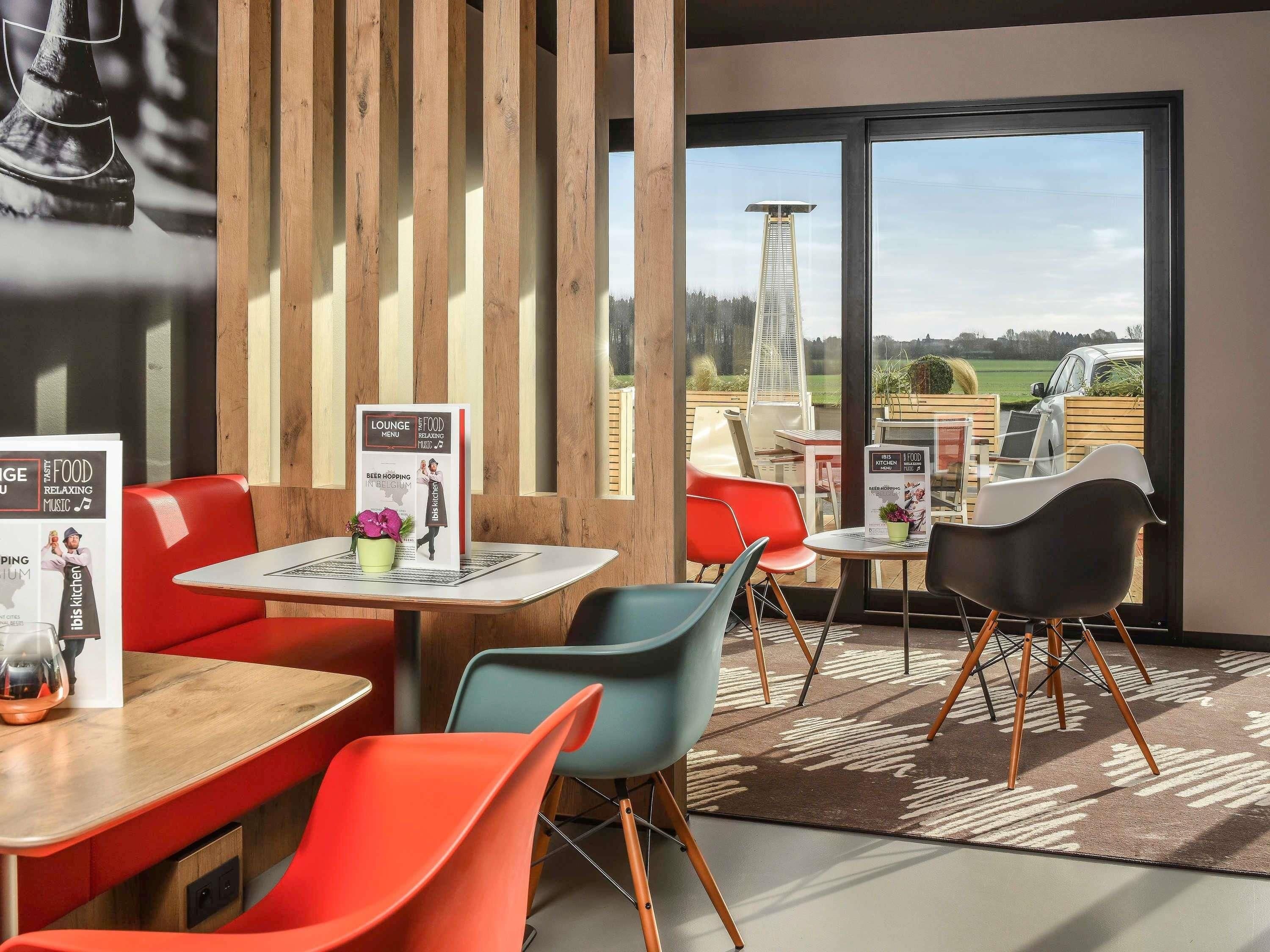 A modern indoor dining area with wooden accents, a view of a tall structure outside, and a menu board on the tables.