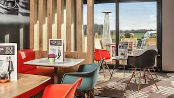 A modern indoor dining area with wooden accents, a view of a tall structure outside, and a menu board on the tables.