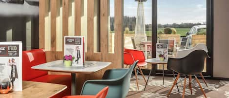 A modern indoor dining area with wooden accents, a view of a tall structure outside, and a menu board on the tables.