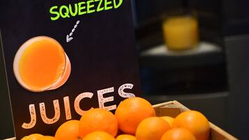 Une enseigne publicitaire pour des jus de fruits fraîchement pressés, avec une caisse en bois remplie d’oranges au premier plan.