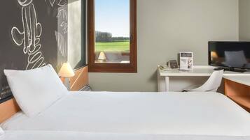 A hotel room with a bed, a desk, a TV, and a window with a view of a field.
