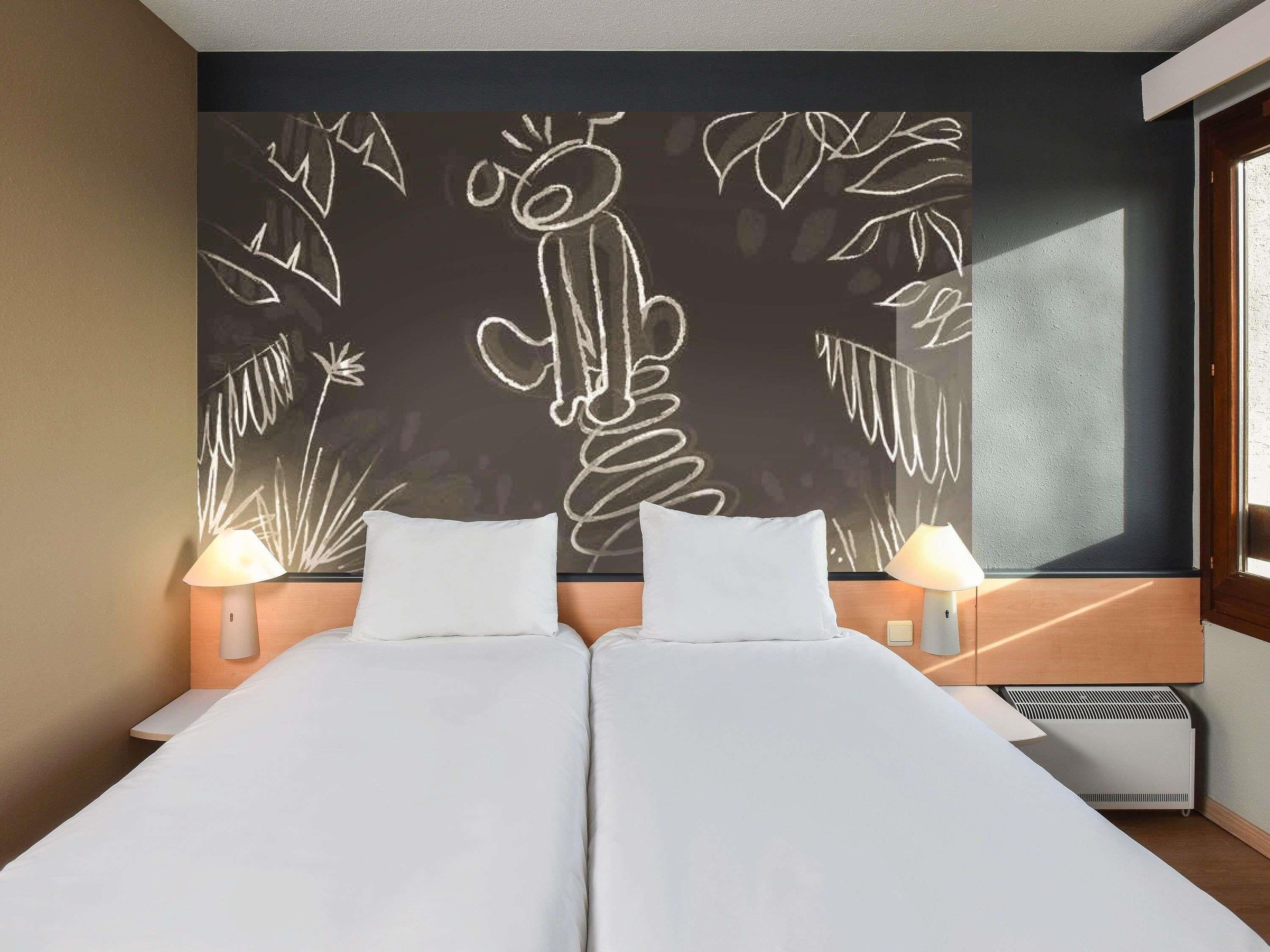 A double bed with white linens, two bedside lamps, and a wall with a chalkboard drawing.