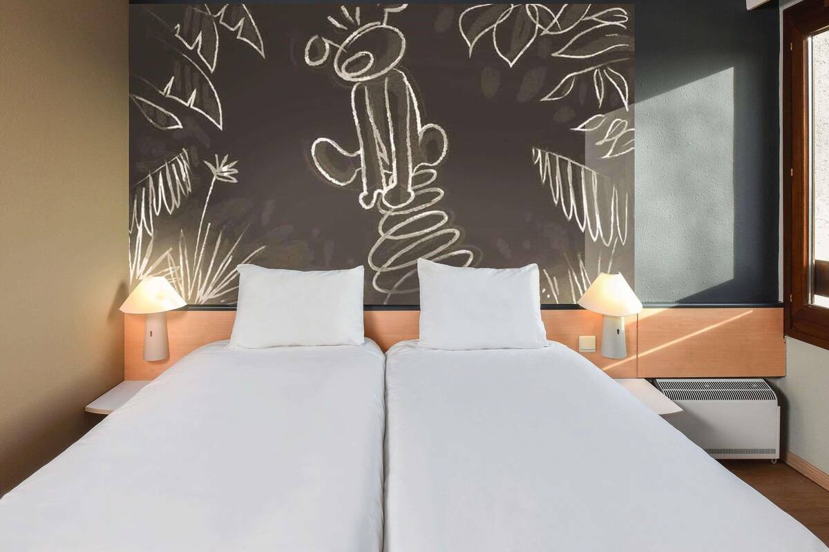 A double bed with white linens, two bedside lamps, and a wall with a chalkboard drawing.