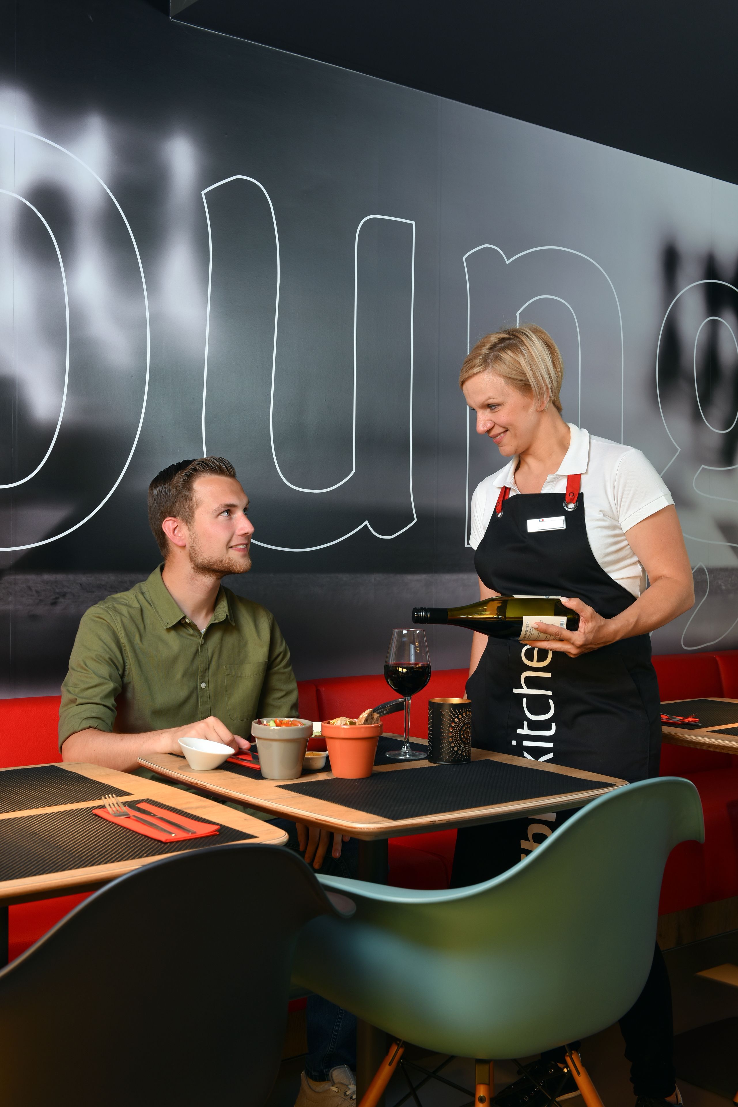 A restaurant interior with a modern design, featuring a black wall with white lettering, wooden tables, and colorful chairs.