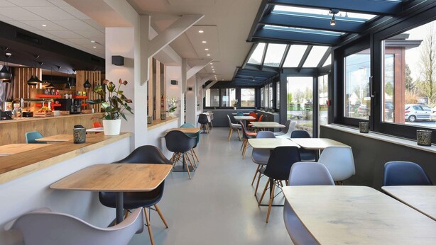 Una cafetería moderna con una barra alargada, zona de estar y grandes ventanales.