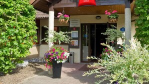 Entrada de un hotel con un cartel que dice 'ibis HOTELS', un acceso cubierto y plantas con flores.