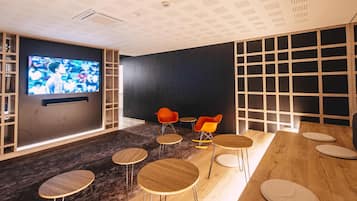 A modern lounge with a TV, wooden tables, and orange chairs.