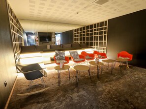 A modern lounge area with a sofa, red chairs, and a coffee table. - ibis Haguenau Strasbourg Nord (Haguenau)