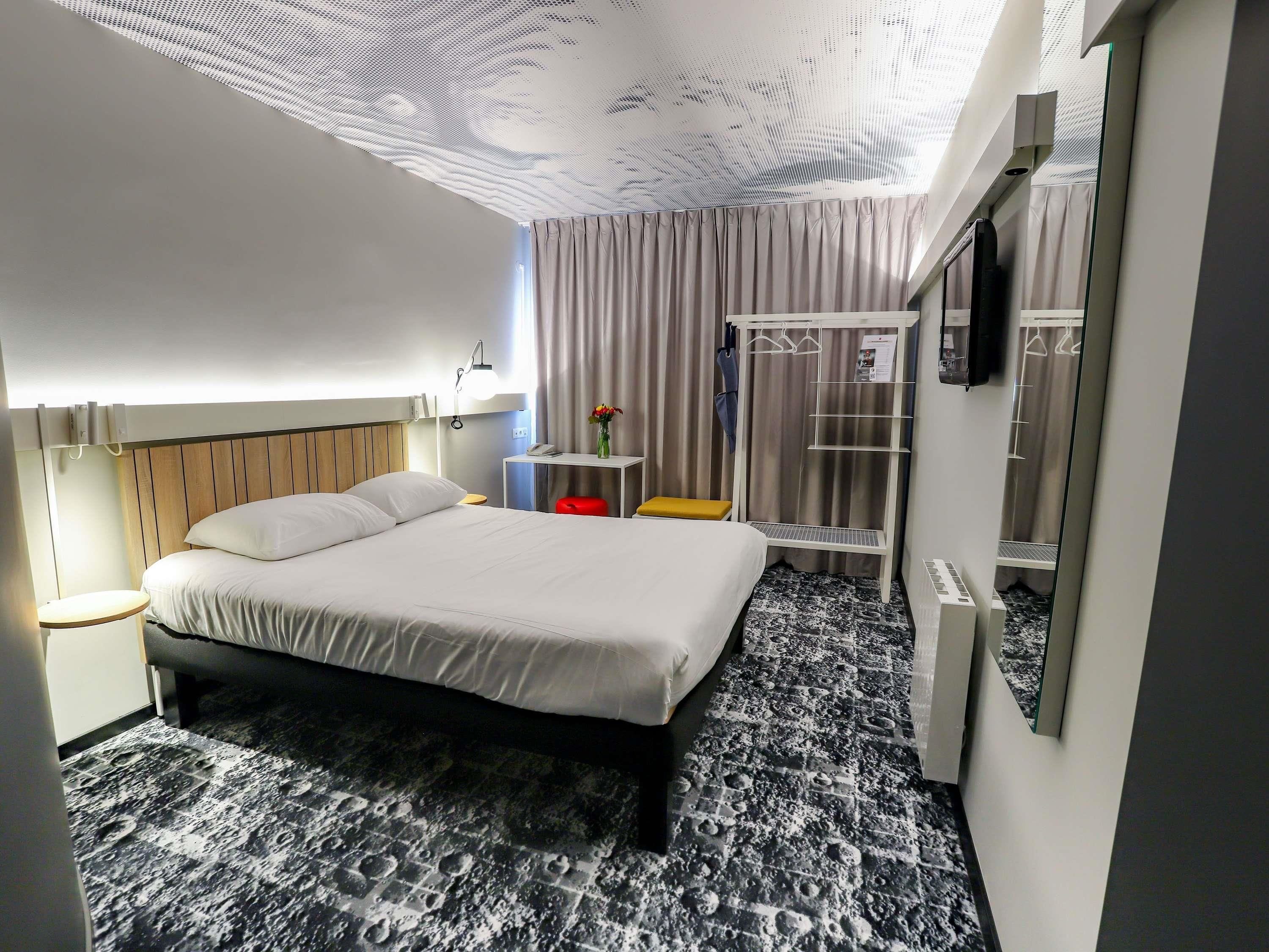 Una habitación de hotel moderna con cama, mesita de noche, lámpara, armario y zona de ducha.