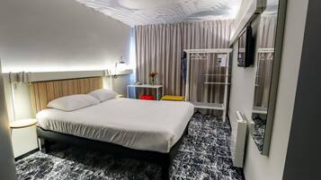Una habitación de hotel moderna con cama, mesita de noche, lámpara, armario y zona de ducha.