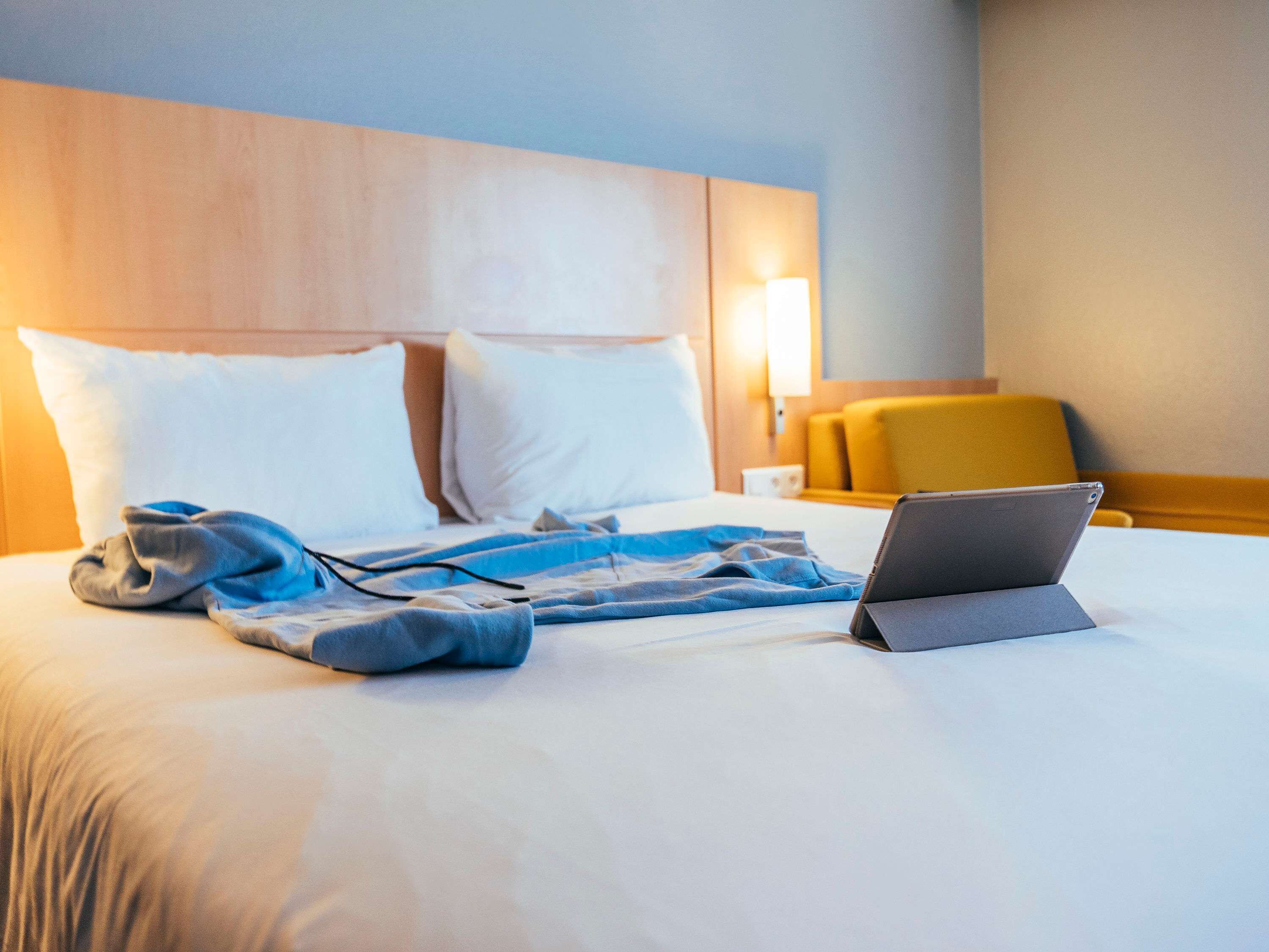 A hotel room with a bed, pillows, a laptop, and a blanket.