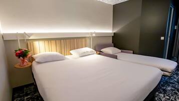 Habitación de hotel con una cama grande, una cama más pequeña, una mesita de noche con un florero y un diseño moderno en el techo.