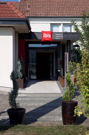 The exterior of a modern hotel with a red sign indicating it is the ibis hotel.