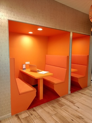 A modern, orange-themed workspace with a wooden table and a laptop, featuring built-in seating and a patterned wall. - ibis Haguenau Strasbourg Nord (Haguenau)