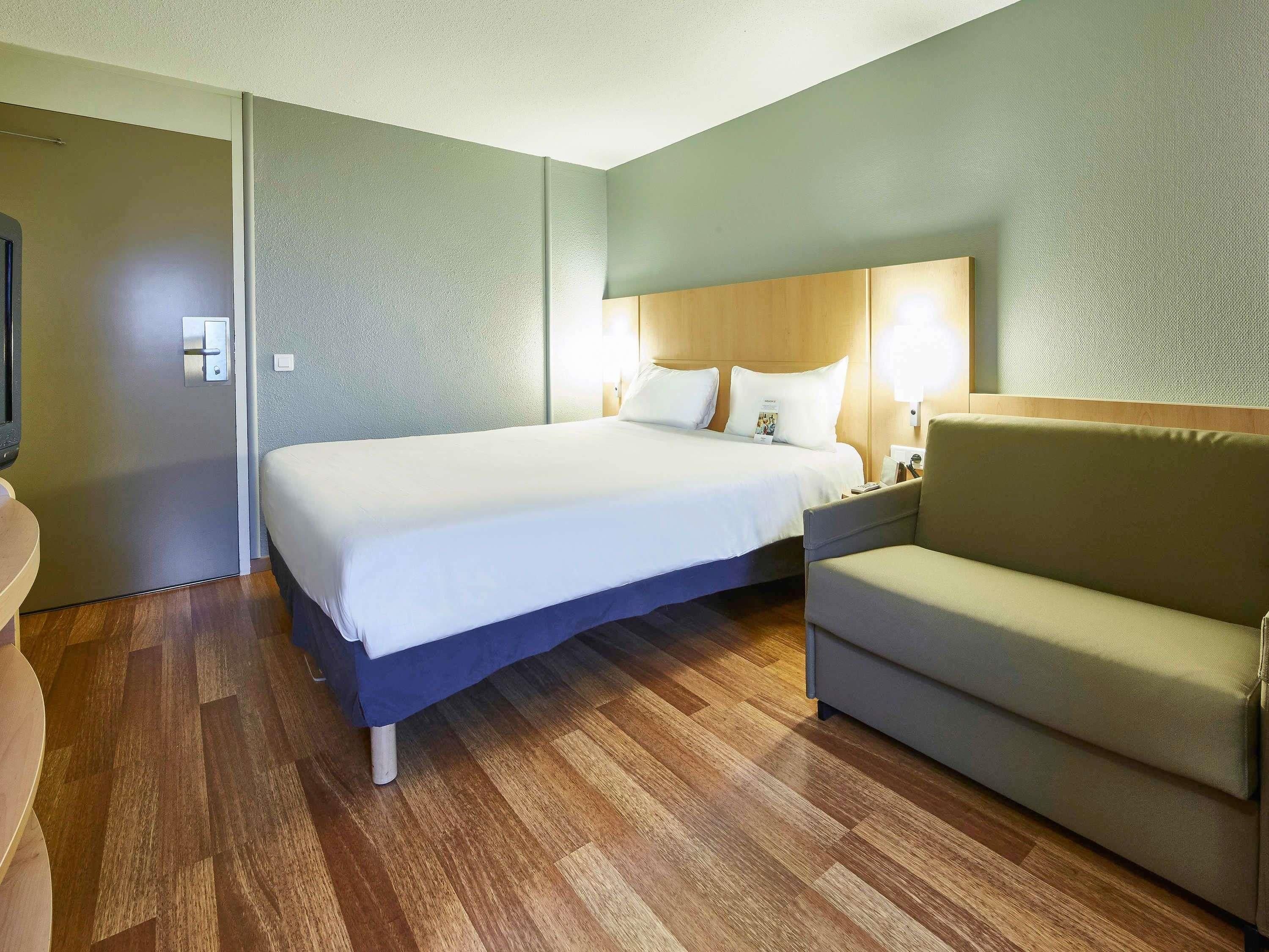 Una camera d'albergo con un letto, un divano, un comodino e una TV a parete.