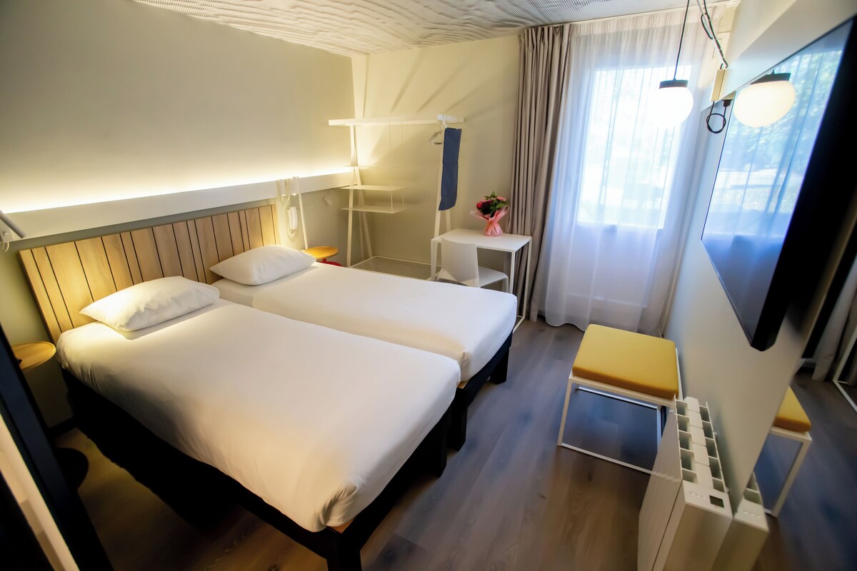 A hotel room with two beds, a small table with a vase of flowers, a desk, and a TV.