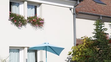 A hotel named "ibis HOTEL" with a tiled roof, outdoor seating with a blue umbrella, and flower boxes on the windows.
