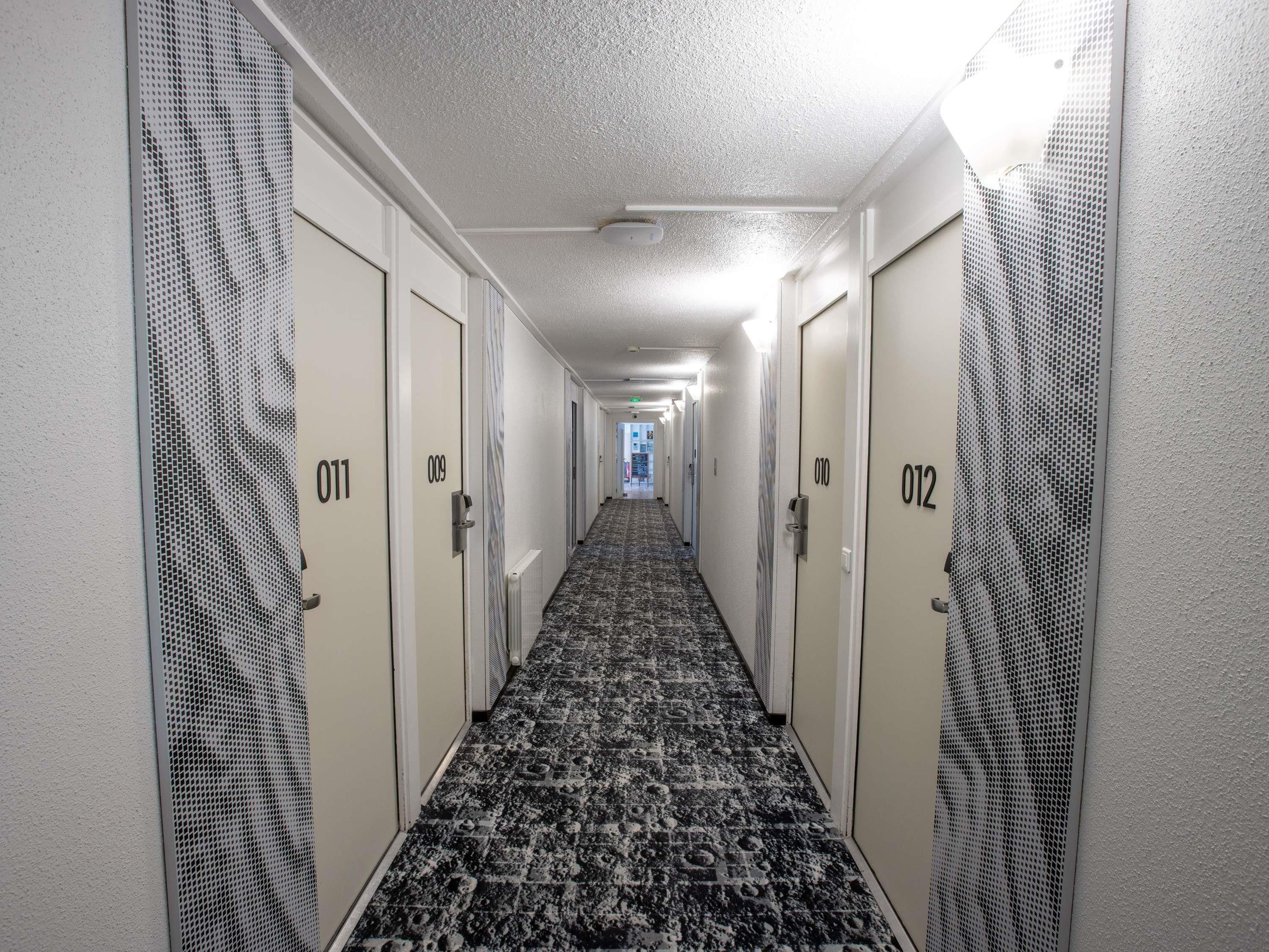A hotel hallway with numbered doors, carpeted floors, and a ceiling with recessed lighting.