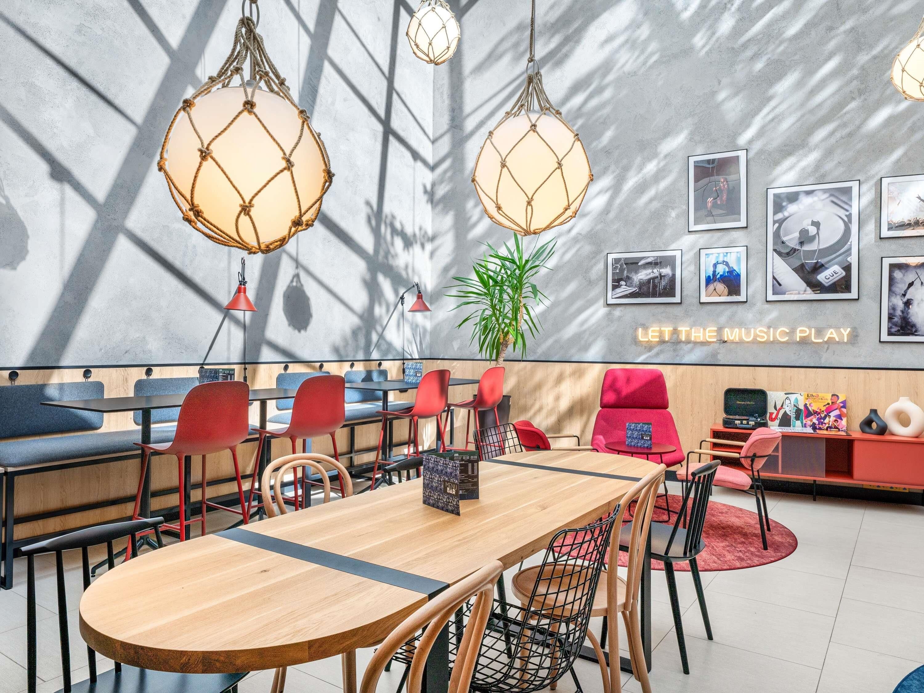 A modern cafe with wooden tables, red chairs, and pendant lights.