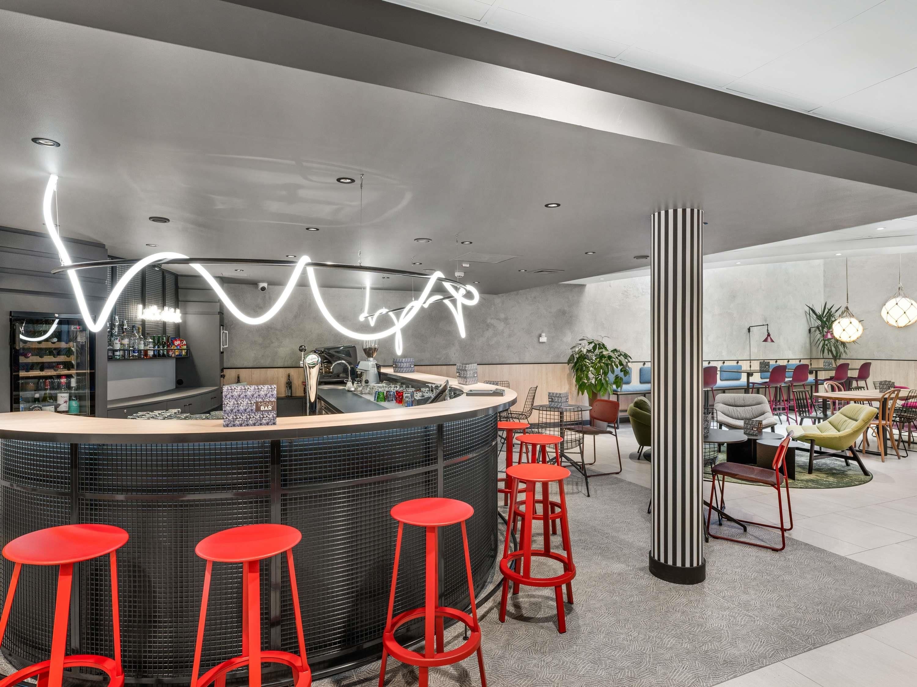 Zona de bar moderna con una barra curva, taburetes rojos y un diseño de luces de neón en el techo.