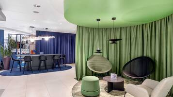 Un interior modern amb una paret verda corba, una zona de bar amb tamborets i una zona d'estar amb una taula rodona i seients.