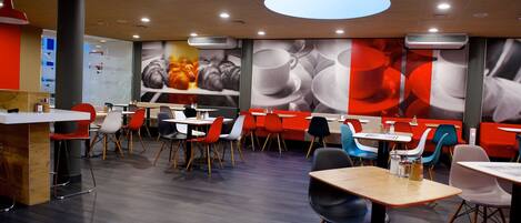 A modern restaurant with a variety of seating options, including tables and chairs, and a large wall mural.