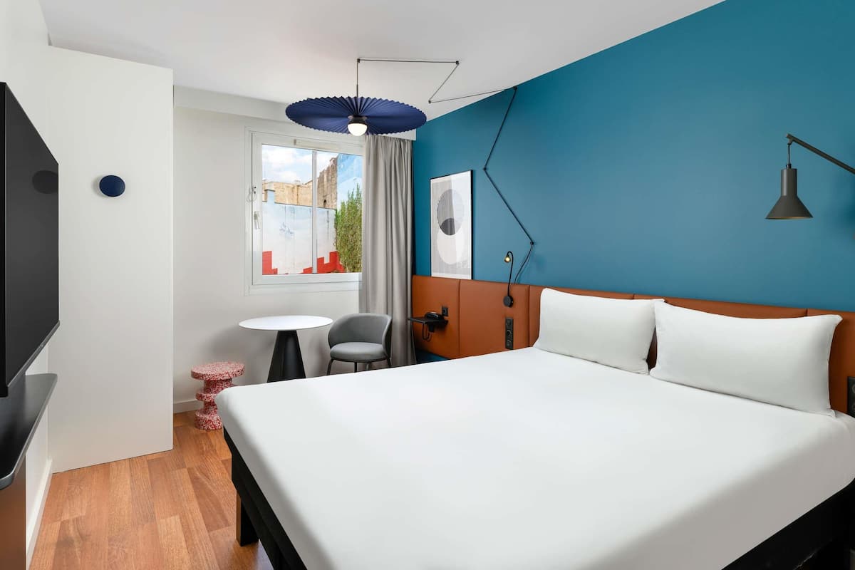 A hotel room with a large bed, a desk, a chair, a TV, and a window with curtains.