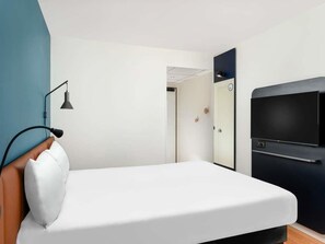 Una habitación de hotel moderna con cama, escritorio, silla, lámpara de escritorio, televisor y puerta.