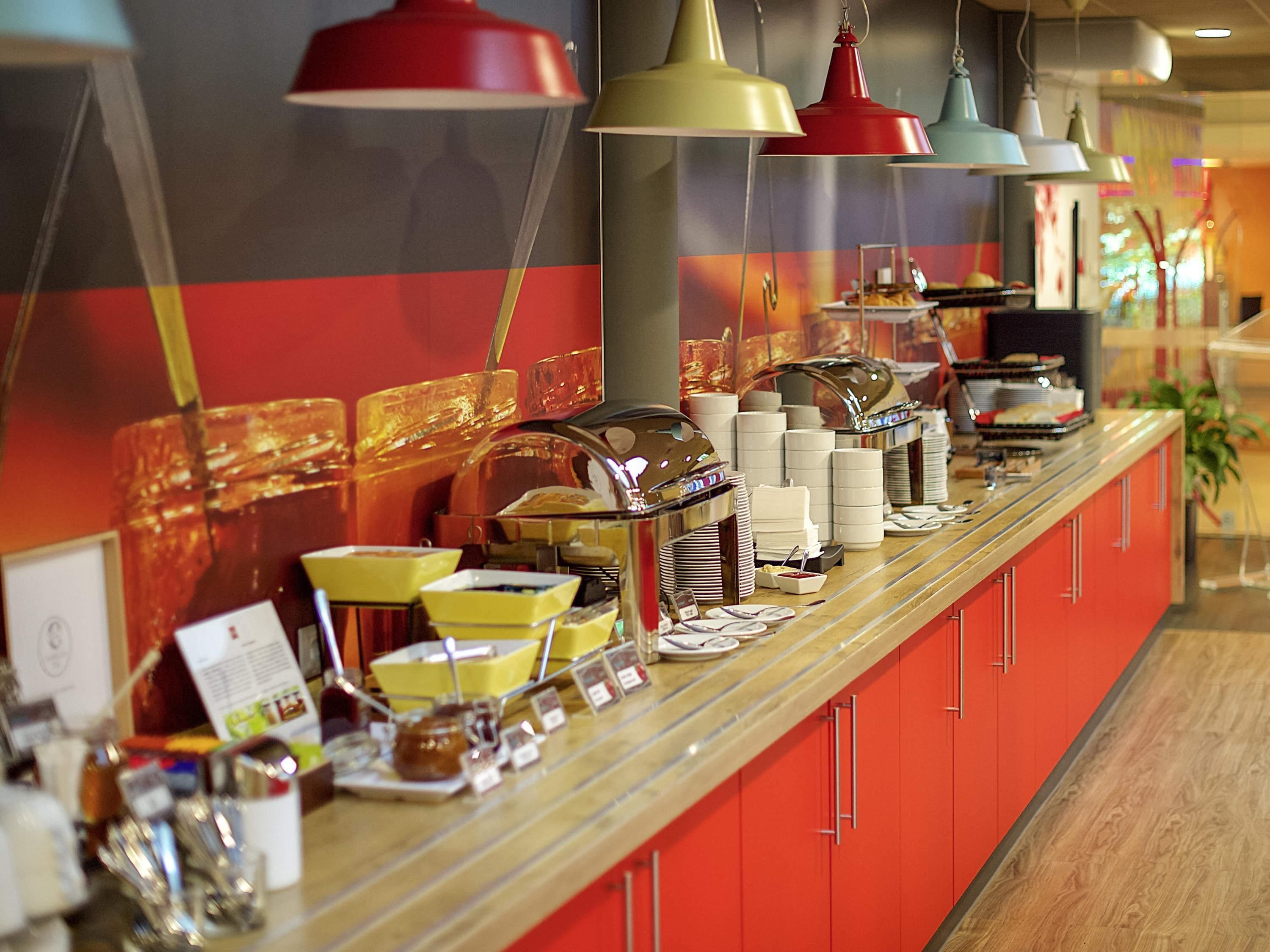 Un comptoir de buffet avec divers plats et ustensiles, une vitrine réfrigérée et des lampes suspendues au plafond.