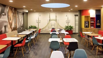 Un restaurante con un mural de un puente, varias mesas y sillas, y un diseño moderno en el techo.