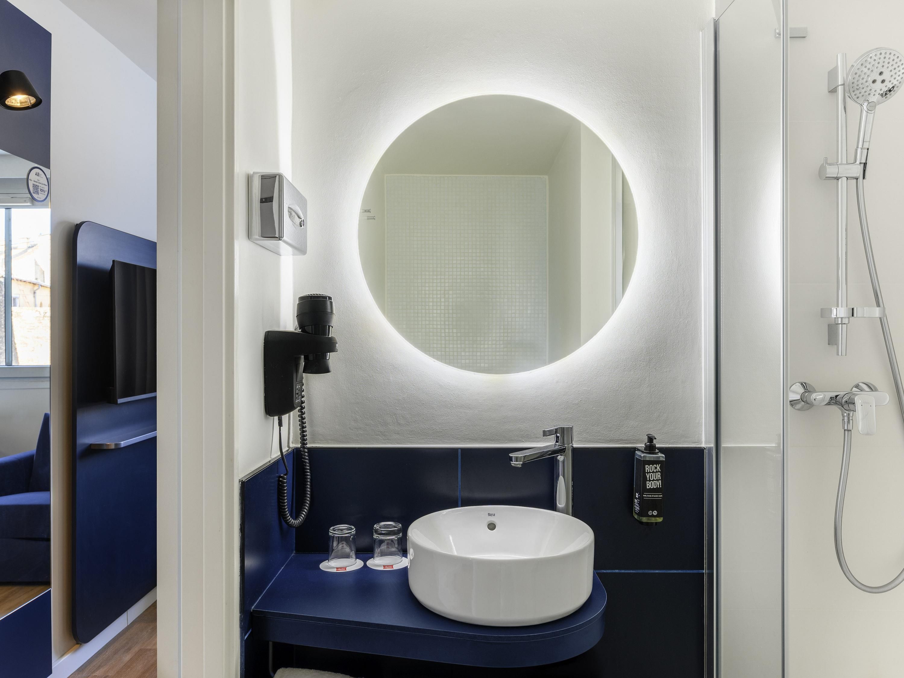 Un baño moderno con un espejo redondo, un lavamanos y una ducha.