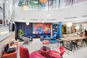 A spacious lobby with a modern design, featuring a large seating area, a DJ setup, and a mural on the back wall.