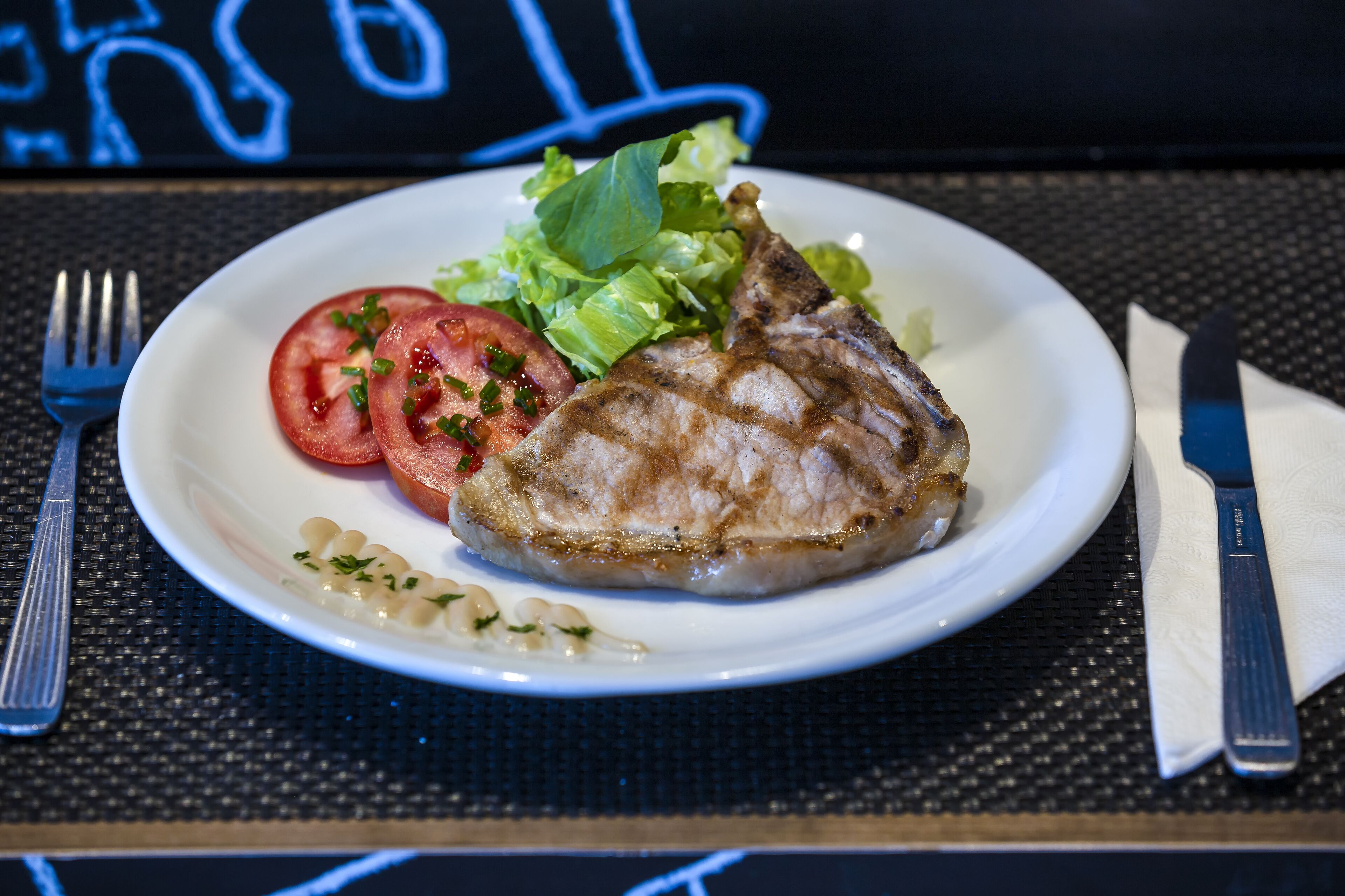 A plate with grilled meat, lettuce, and tomato slices on a black tablecloth.