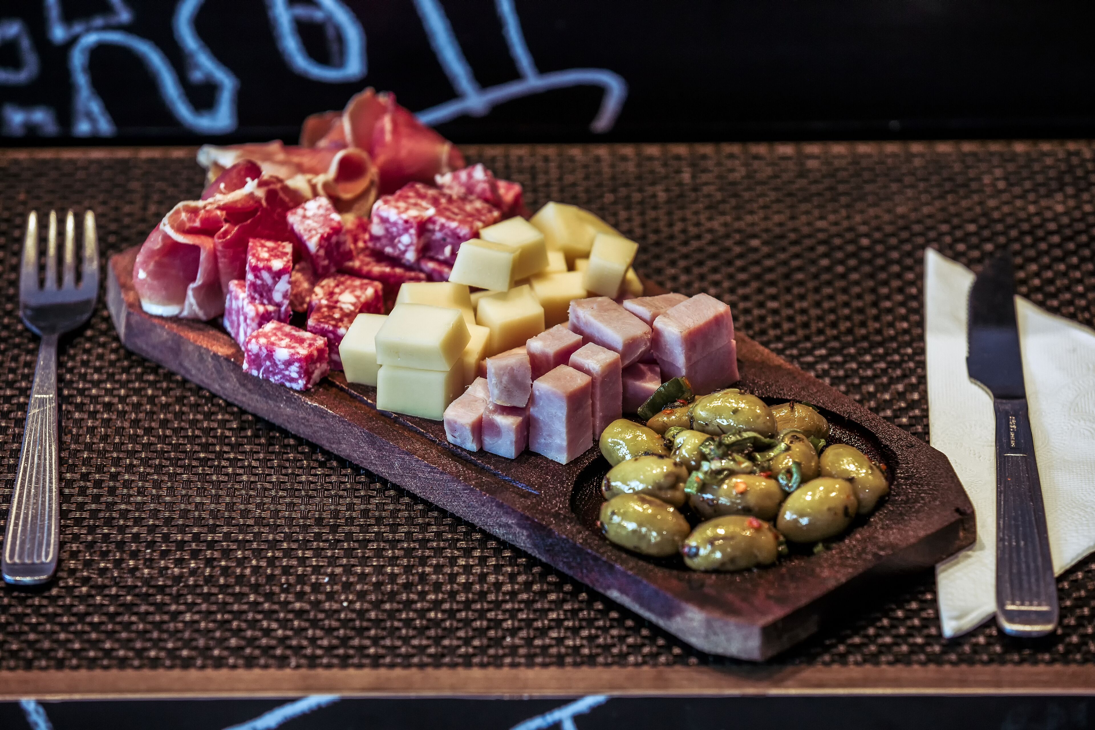 A charcuterie board with various meats, cheeses, and olives on a wooden board.