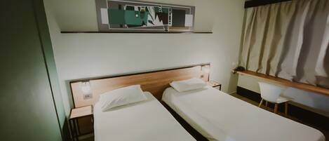 A hotel room with two single beds, a desk, a chair, a mirror, and a window with curtains.