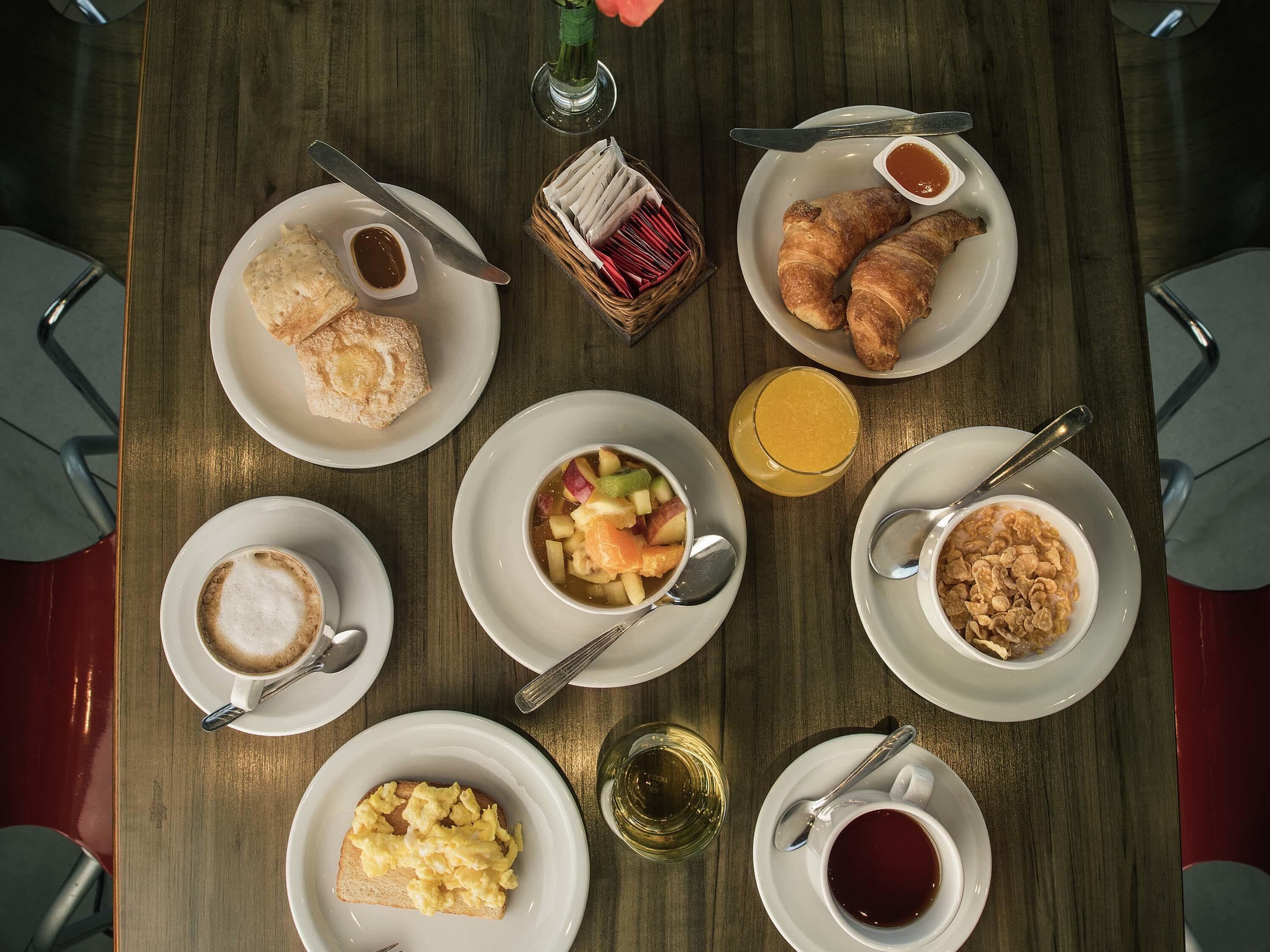 Desayuno con croissants, fruta, café y cereal sobre una mesa de madera.
