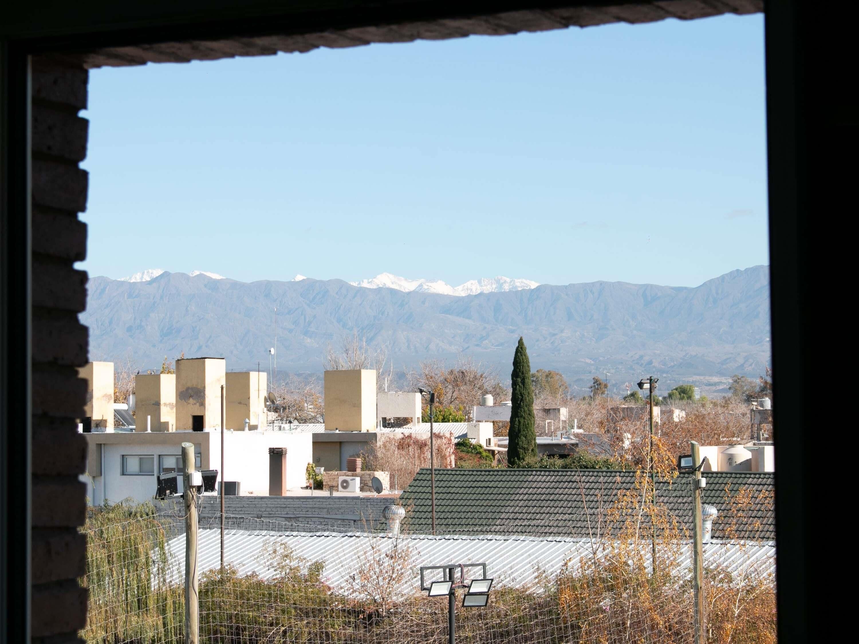 Un barrio residencial con edificios, una cancha deportiva cercada y una cadena montañosa al fondo.