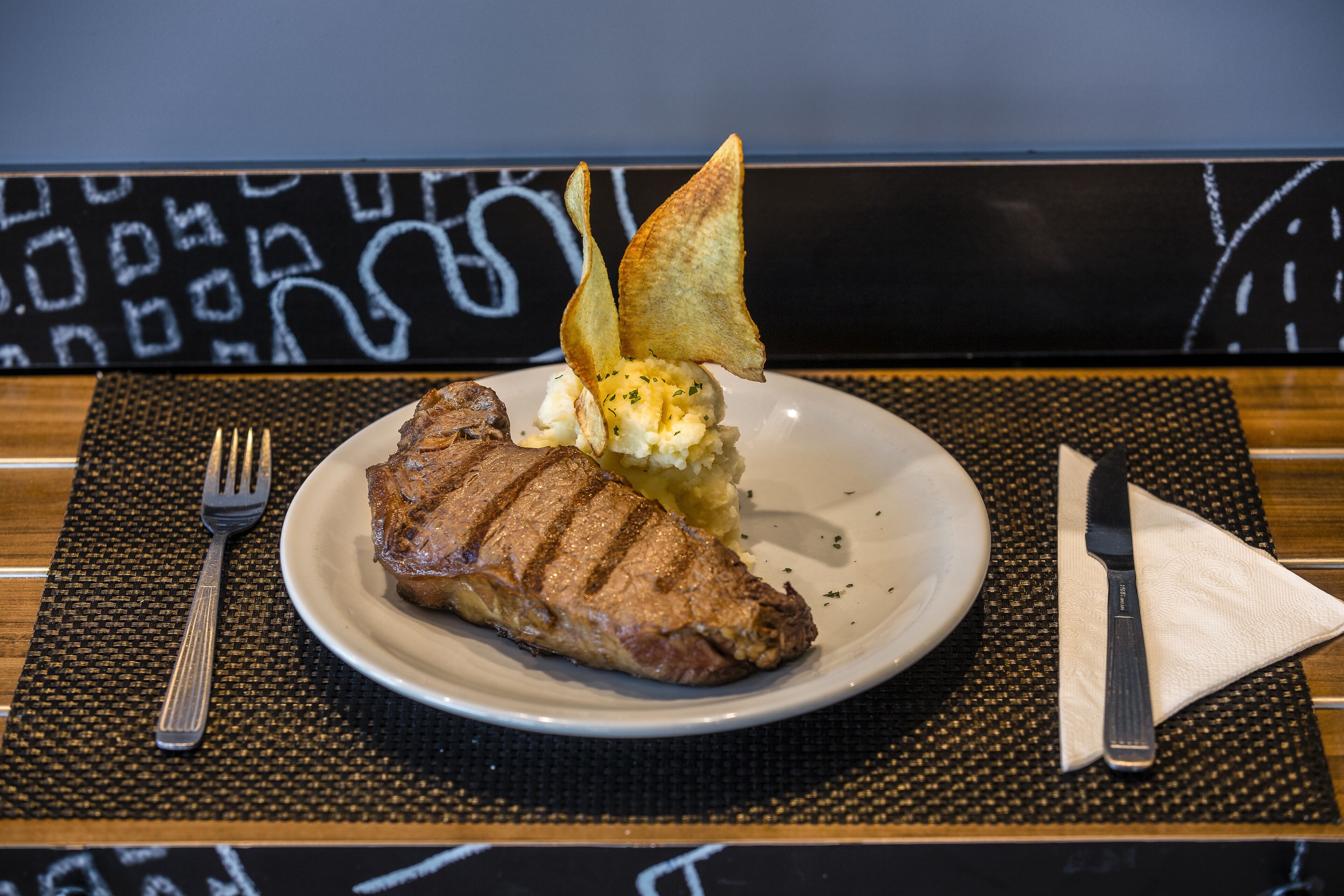 A plate with a grilled steak, mashed potatoes, and a garnish on a black and white patterned tablecloth.